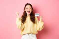兴奋年轻的女人赢得奖太棒了促销出售显示塑料信贷卡尖叫快乐站粉红色的背景