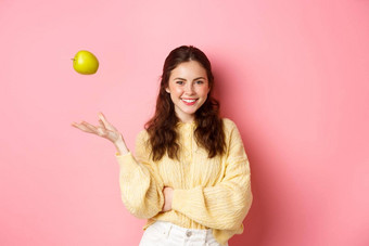 年轻的微笑女人信心扔苹果空气吃健康的水果微笑完美的站粉红色的背景