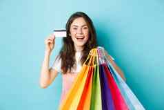快乐美丽的女人显示塑料信贷卡购物袋货物购买折扣站蓝色的背景