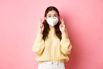 科维德封锁流感大流行概念年轻的女人充满希望的使交叉手指穿医疗面具呼吸器冠状病毒粉红色的背景