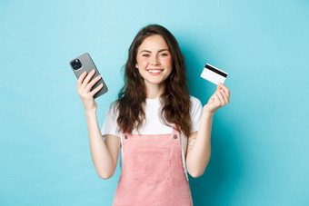 微笑可爱的女孩显示塑料信贷卡智能手机订单商店移动应用程序商店在线支付订单站蓝色的背景