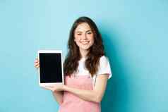 肖像微笑美丽的女人演示空白平板电脑屏幕显示促销设备屏幕站蓝色的背景