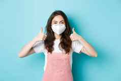 科维德健康流感大流行概念图像可爱的年轻的女人呼吸器显示拇指思考个人安全封锁检疫穿脸面具蓝色的背景