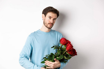 英俊的年轻的男人。持有美丽的红色的玫瑰情人情人节一天沉思的站白色背景