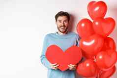 微笑的男朋友持有情人节卡站浪漫的红色的心气球庆祝情人一天站白色背景