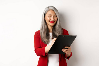 成功的亚洲高级女商人灰色头发采取笔记剪贴板检查企业站白色背景