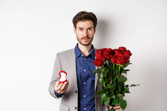 英俊的男人。西装使建议站红色的玫瑰花订婚井盒子使浪漫的惊喜白色背景