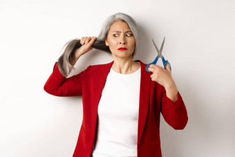 优柔寡断亚洲女人持有剪刀怀疑思考减少头发改变发型站白色背景