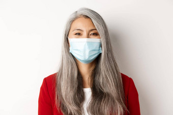 科维德流感大流行业务概念特写镜头快乐的亚洲高级女商人医疗面具微笑相机白色背景
