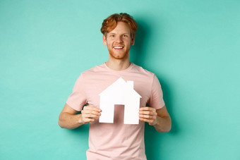 真正的房地产概念年轻的男人。红色的头发穿t恤显示纸房子断路微笑快乐站薄荷背景