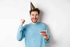 庆祝活动假期概念快乐的年轻的男人。庆祝生日聚会，派对他持有bday蛋糕快乐站白色背景