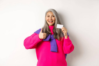 购物概念微笑亚洲中年女人灰色头发显示塑料信贷卡竖起大拇指推荐银行促销活动白色背景