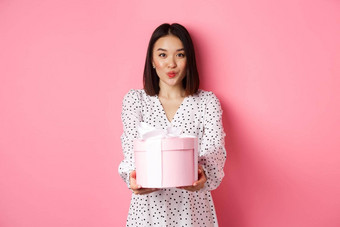 可爱的亚洲女朋友祝贺情人节一天给可爱的浪漫的礼物盒子皱纹嘴唇吻站粉红色的背景