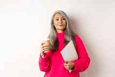 时尚的亚洲高级女商人喝咖啡持有移动PC自信沾沾自喜相机站白色背景
