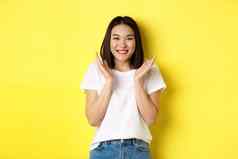 美时尚概念兴奋亚洲女人鼓掌手微笑快乐相机站白色t恤黄色的背景