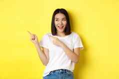 美时尚概念美丽的亚洲女人白色t恤指出手指左站黄色的背景