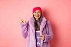 时尚购物概念快乐亚洲高级女人检查时尚的促销活动指出手指左标志微笑穿冬天假的皮毛外套头巾