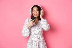 美丽的微笑亚洲女人唱歌首歌智能手机麦克风玩卡拉ok应用程序耳机站粉红色的背景