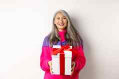 美丽的亚洲高级女人微笑祝贺情人节一天持有礼物盒子站白色背景