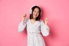 快乐年轻的亚洲女人跳舞有趣的听音乐耳机站粉红色的背景