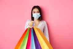 科维德流感大流行生活方式概念美丽的亚洲女人脸面具给购物袋社会距离商店站粉红色的背景
