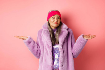 时尚时髦的亚洲女人耸肩膀困惑笨站时尚的紫色的外套头巾粉红色的背景
