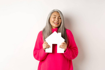真正的房地产美丽的梦幻亚洲夫人拥抱纸房子模型关闭眼睛微笑做梦购买公寓站白色背景