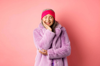 时尚购物快乐亚洲成熟的女人紫色的人造皮毛外套微笑可爱的无忧无虑的关闭眼睛幸福站粉红色的背景