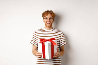 情人节一天假期概念快乐的年轻的男人。持有礼物盒子微笑感激的接收礼物站白色背景