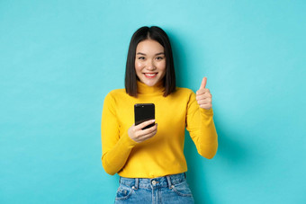 <strong>电子</strong>商务在线购物概念满意亚洲女客户端显示拇指智能<strong>手机</strong>微笑很高兴相机蓝色的背景