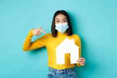 科维德流感大流行真正的房地产概念快乐的亚洲女人微笑医疗面具显示纸房子断路推荐机构购买财产蓝色的背景