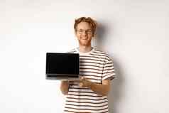 微笑骄傲红色头发的人的家伙显示空移动PC屏幕英俊的年轻的男人。展示标志电脑显示白色背景