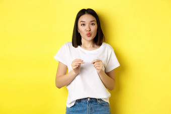 年轻的亚洲女人休闲白色t恤显示塑料信贷卡皱<strong>纹嘴唇</strong>愚蠢的购物黄色的背景
