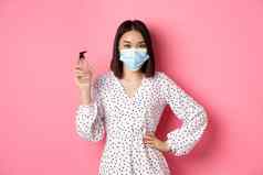 科维德流感大流行生活方式概念美丽的朝鲜文女人衣服医疗面具显示手洗手液推荐防腐剂站粉红色的背景
