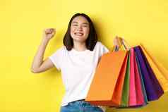 快乐亚洲女人感觉满意购物出售持有纸袋伸展运动很高兴微笑站黄色的背景