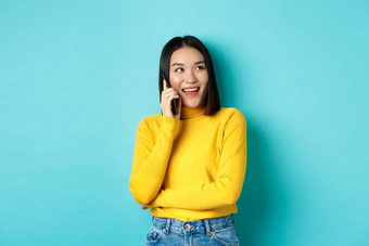 时尚的朝鲜文女人调用电话会说话的智能手机快乐上角落里微笑无忧无虑的站放松构成蓝色的背景