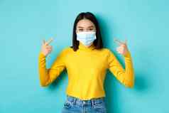 科维德社会距离流感大流行概念年轻的亚洲女人保护冠状病毒指出手指医疗面具站蓝色的背景