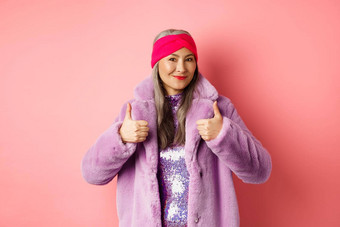 时尚购物概念亚洲时尚夫人冬天外套显示竖起大拇指微笑满意推荐公司促销粉红色的背景