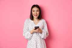 可爱的亚洲女人思考微笑左梦幻消息传递智能手机勃朗宁在线商店站粉红色的背景