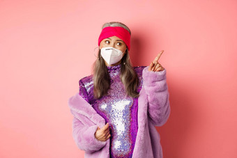 冠状病毒购物概念时髦的上了年纪的亚洲女人呼吸器闪闪发光的闪亮的衣服指出上角落里怀疑粉红色的背景