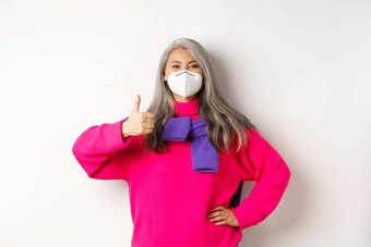 科维德流感大流行社会距离概念快乐的亚洲高级女人呼吸器显示竖起大拇指穿脸面具冠状病毒白色背景