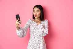 美丽的亚洲女孩照片过滤器应用程序采取自拍智能手机摆姿势可爱的衣服粉红色的背景