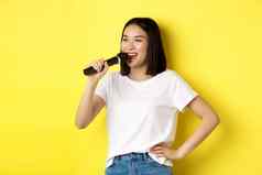快乐亚洲女人唱歌首歌卡拉ok持有麦克风快乐的微笑站黄色的背景