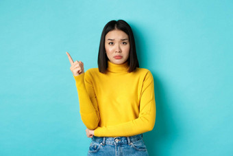 购物概念伤心悲观的亚洲女孩黄色的毛衣指出手指左皱着眉头显示坏<strong>新闻</strong>复制空间站<strong>蓝色</strong>的背景