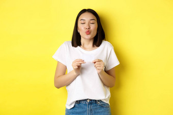 年轻的亚洲女人休闲白色t恤显示塑料信贷卡皱<strong>纹嘴唇</strong>愚蠢的购物黄色的背景