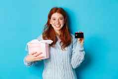 快乐红色头发的人女孩购买礼物信贷卡持有盒子现在微笑站蓝色的背景