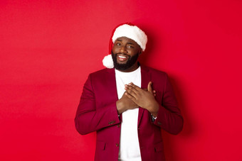 圣诞节聚会，派对假期概念感激的非洲美国男人。圣诞老人他持有手心微笑感觉感动了站红色的背景