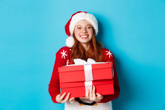快乐假期圣诞节概念快乐的青少年女孩红色的头发穿圣诞老人他持有圣诞节礼物