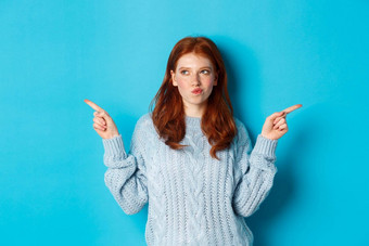 冬天假期人概念深思熟虑的红色头发的人女孩使决定指出手指横盘整理选择方法站蓝色的背景