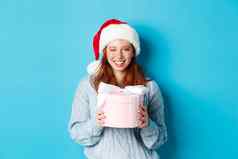 冬天假期圣诞节夏娃概念可爱的红色头发的人女孩毛衣圣诞老人他持有一年礼物相机站蓝色的背景